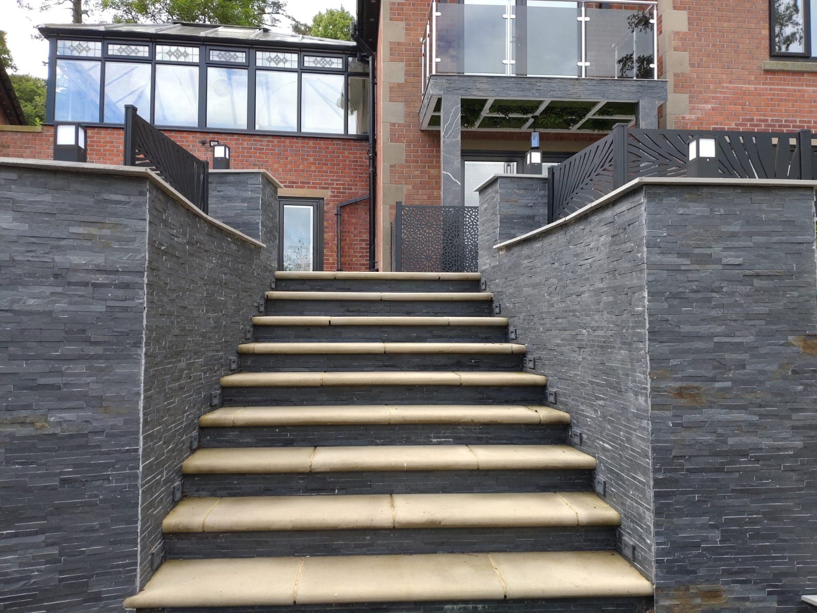 Slate-clad staircase with sandstone treads leading up to a contemporary brick house