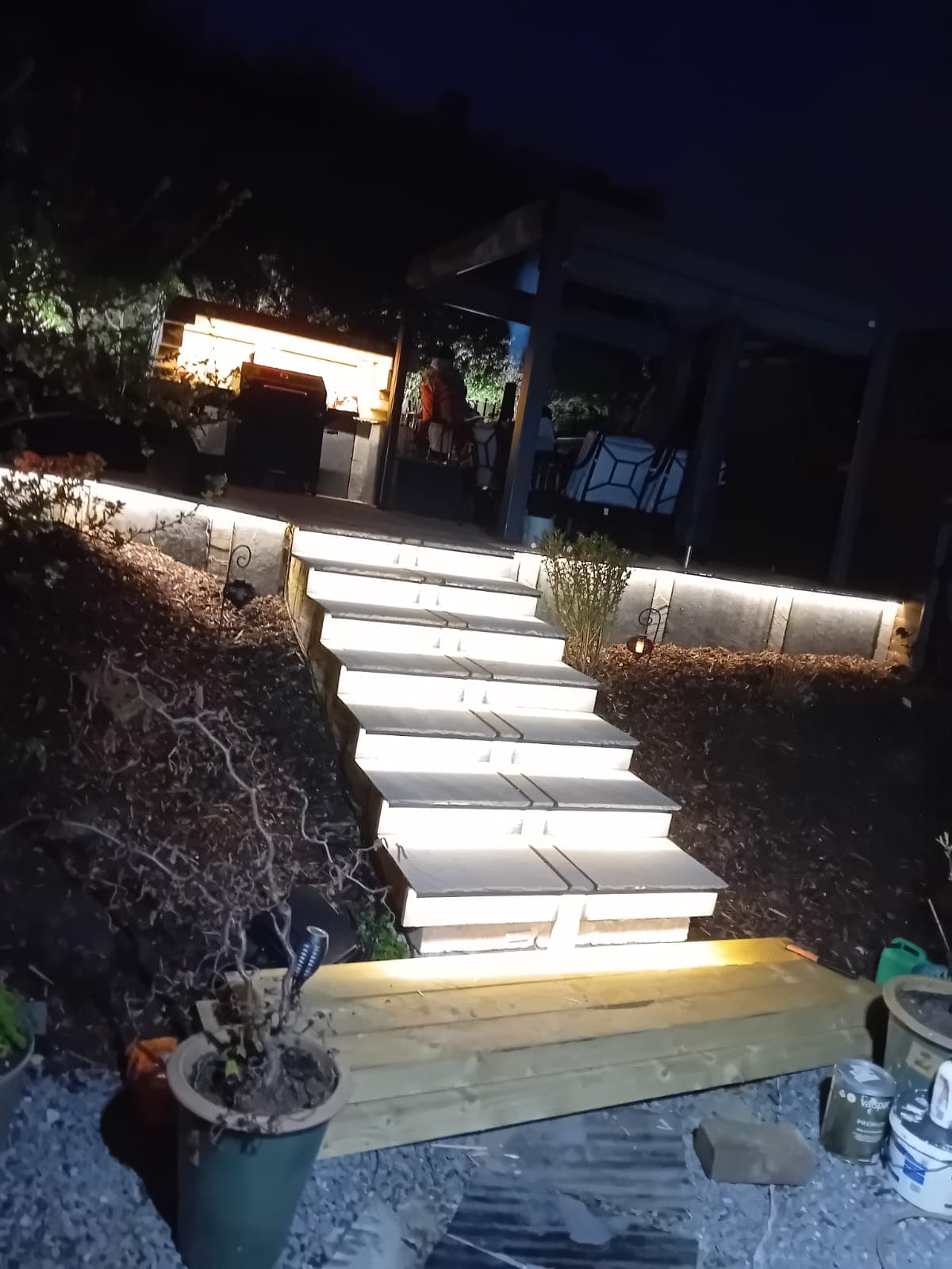 Lit stone patio steps at night leading to a covered outdoor kitchen