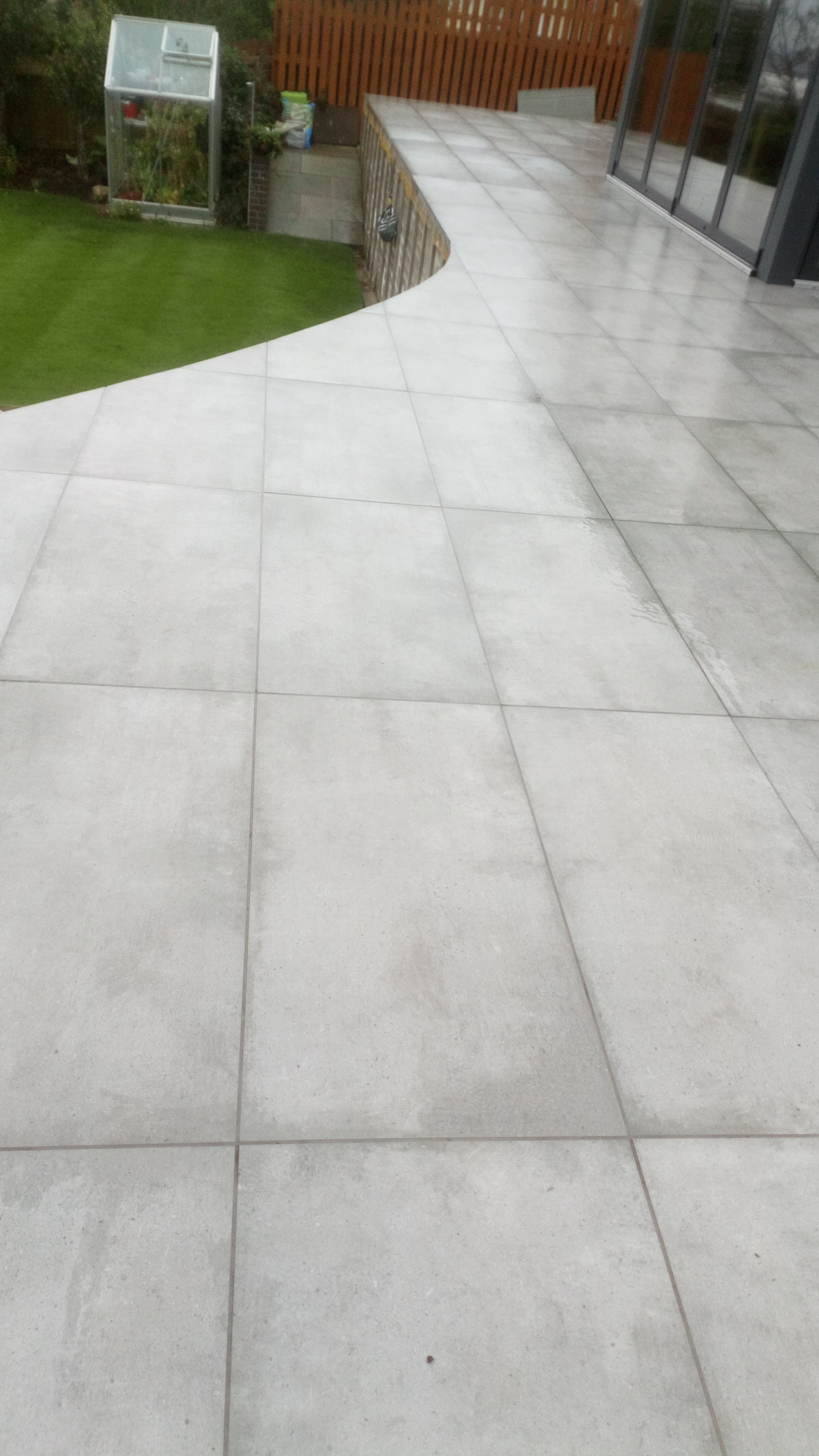 Curved porcelain patio finished, view showing the sweep with greenhouse and lawn