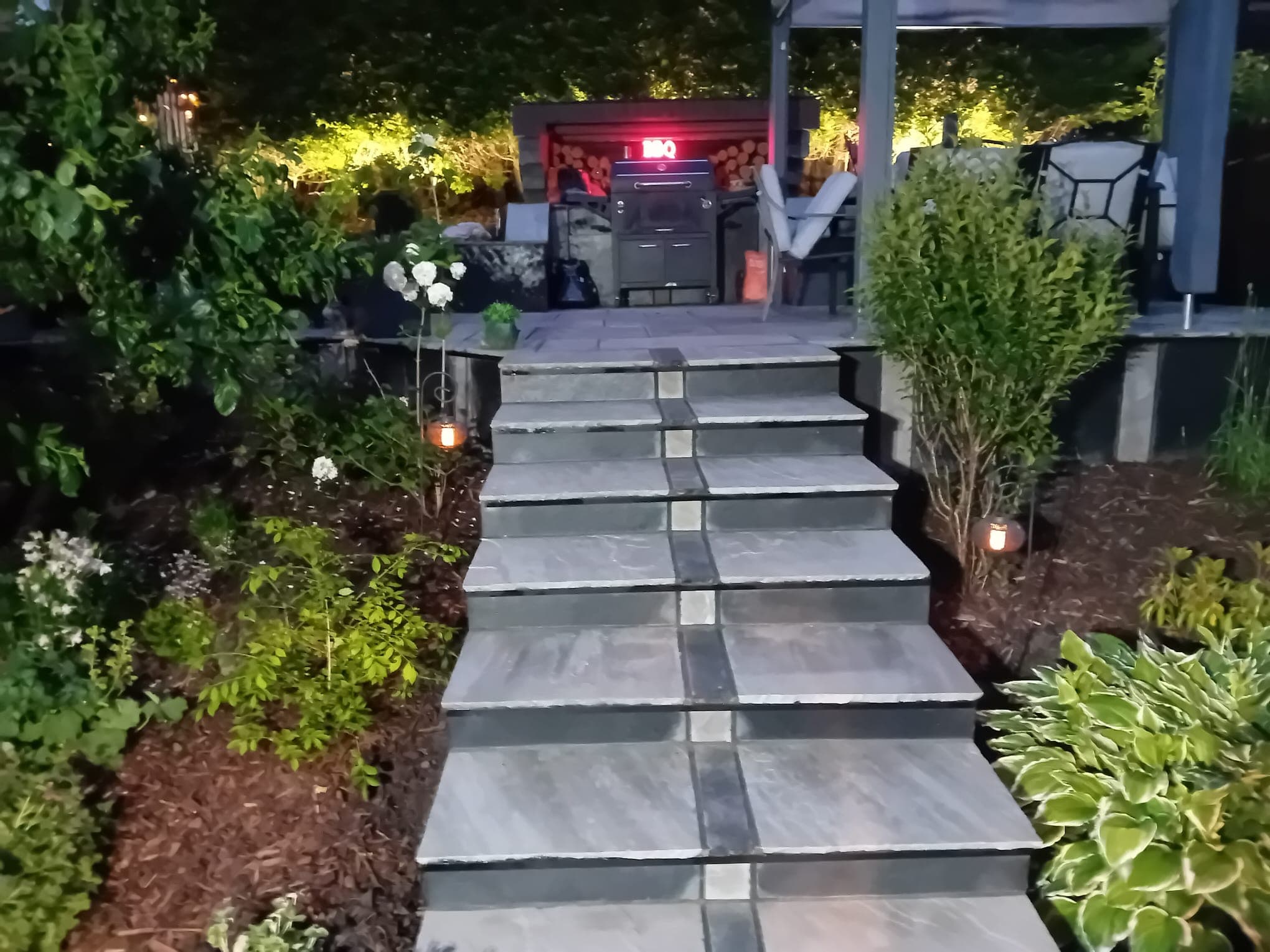 Close-up of the lit stepped flagstone path at night — alternating bands of light and dark stone leading up to the covered outdoor kitchen