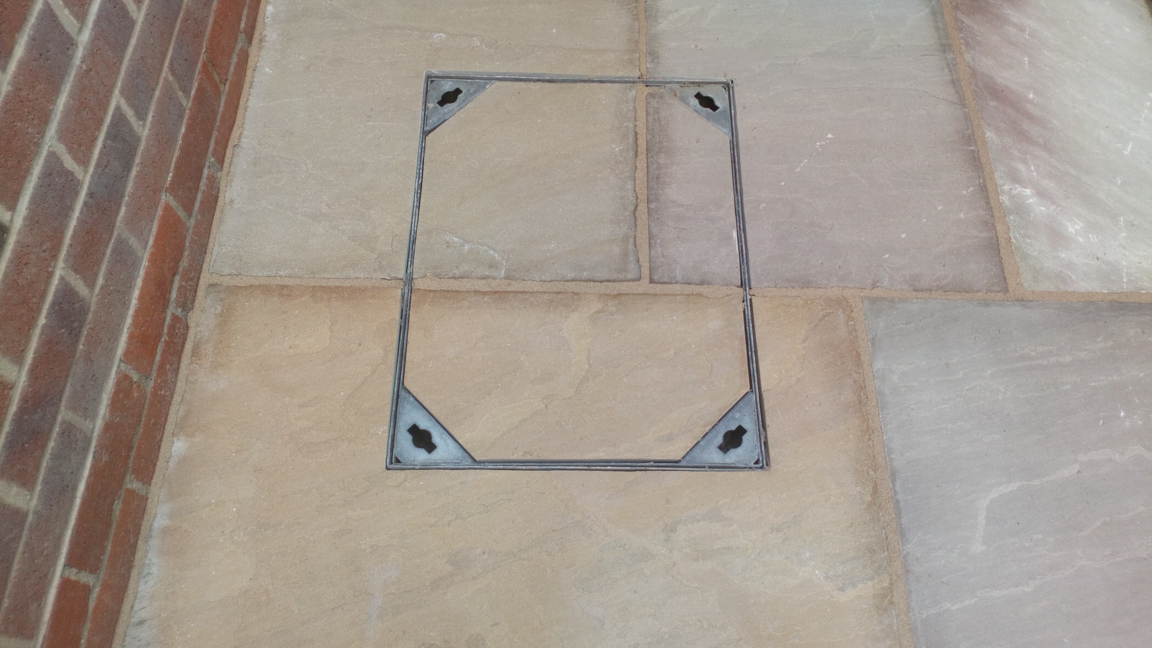 Recessed manhole tray cover in Indian sandstone with brick edging