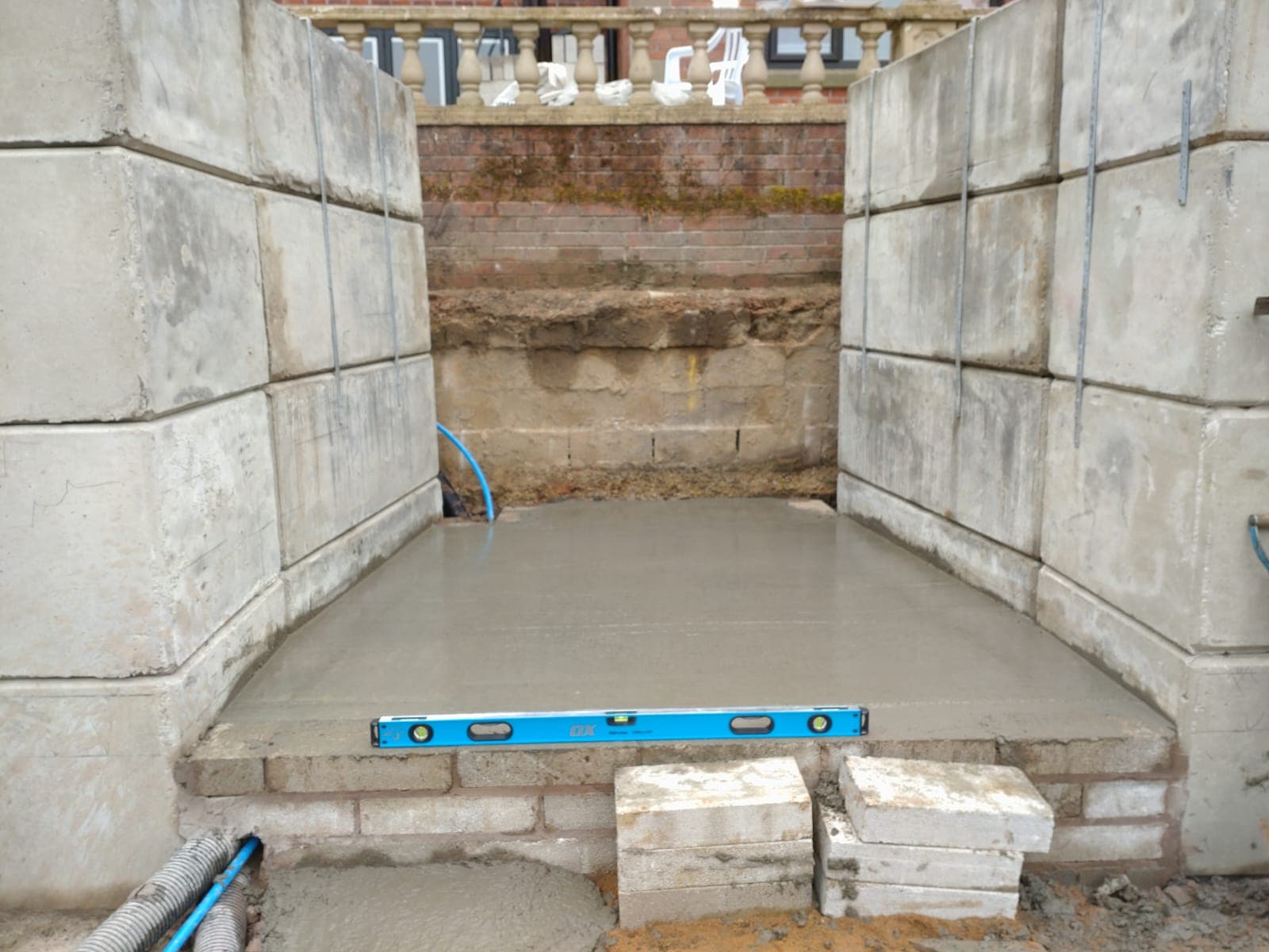 Concrete foundation pour between concrete-block retaining walls, spirit level on the wet base