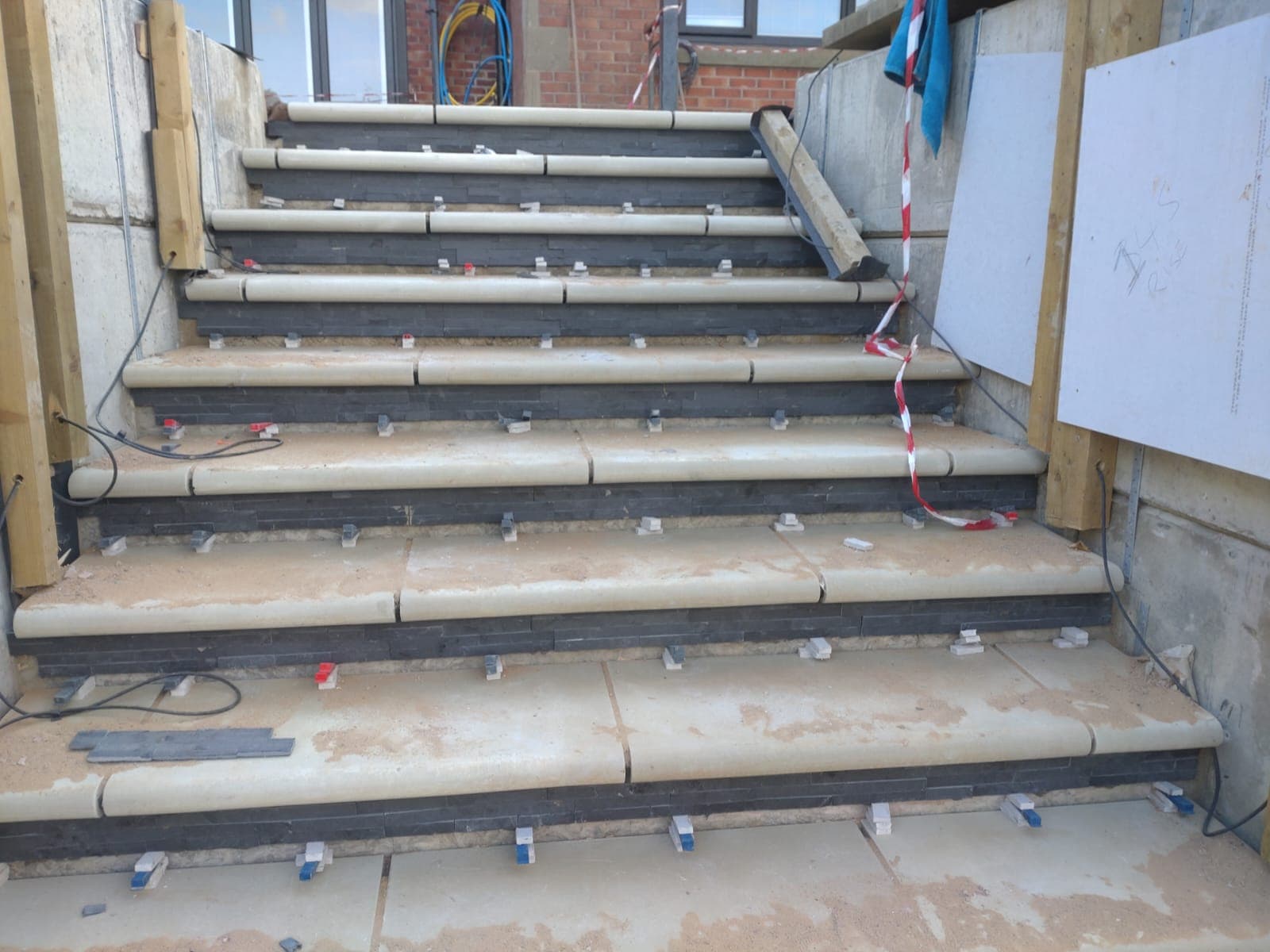 Close-up of slate staircase under construction with levelling clips and spacers visible on every tread